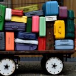 Colorful suitcases of various sizes hastily packed on an old rusty cart next to a wooden wall.