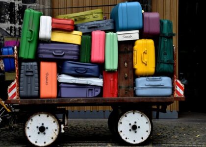 Colorful suitcases of various sizes hastily packed on an old rusty cart next to a wooden wall.