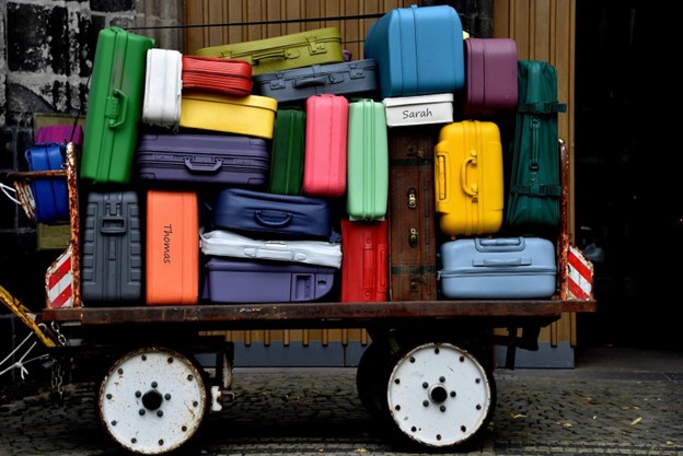 Colorful suitcases of various sizes hastily packed on an old rusty cart next to a wooden wall.