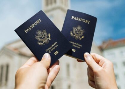 Two hands holding U.S. passports with a building in the background