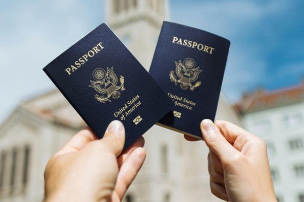 Two hands holding U.S. passports with a building in the background